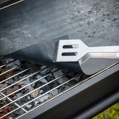 Nahaufnahme einer schwarzen Grillmatte auf dem Rost mit einem Pfannenwender