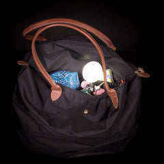 Weiße Lyhton-LED-Leuchte in einer Handtasche mit verschiedenen Gegenständen