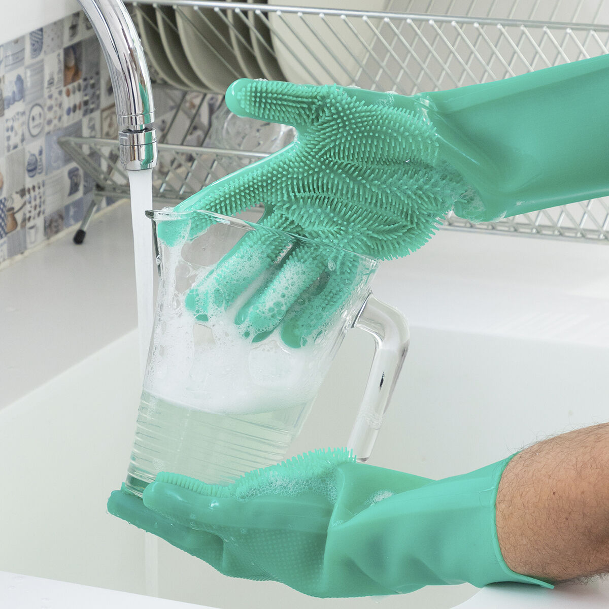 Grüne Silikonhandschuhe reinigen einen Behälter unter fließendem Wasser