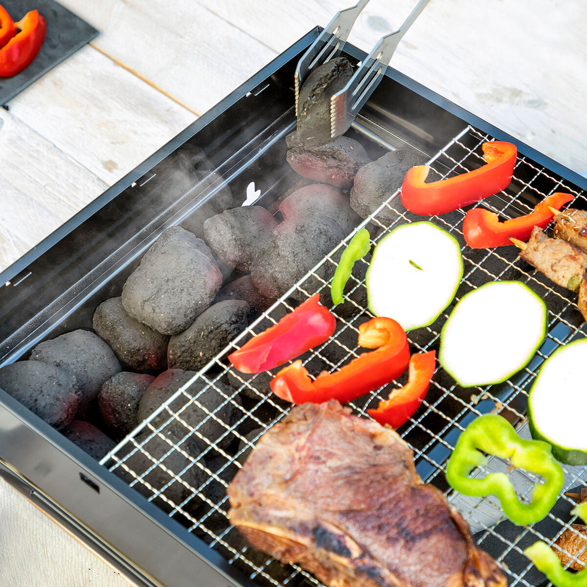 Holzkohle wird bei abgenommenem Grillrost im BearBQ-Grill nachgelegt