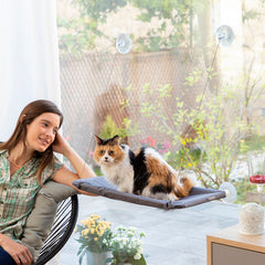 Katze auf der Catlax Fensterliege neben einer sitzenden Frau