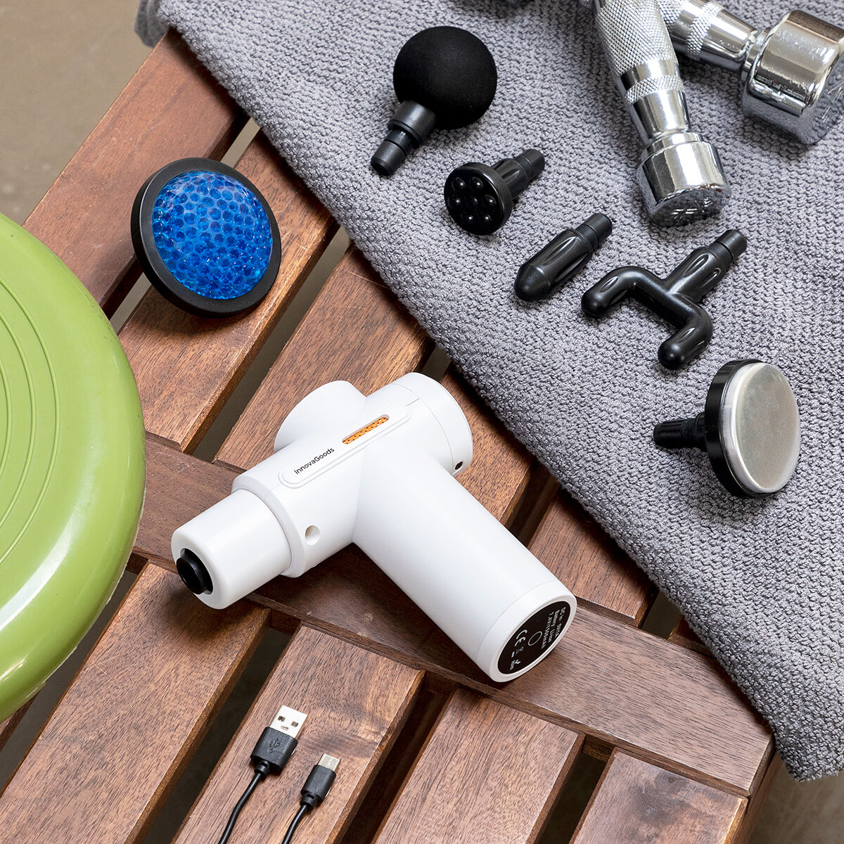 Weiße Hokgun-Massagepistole mit sechs Aufsätzen und USB-Kabel, daneben Trainingsgegenstände