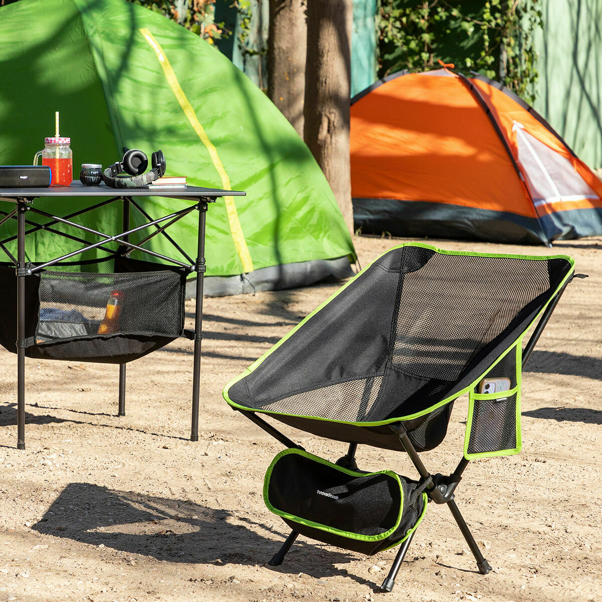 Aufgebauter grün-schwarzer Folstul Campingstuhl auf Gras mit weiteren Campinggegenständen im Hintergrund