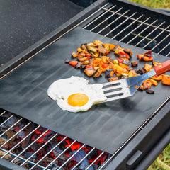Grillmatte auf einem Rost mit Ei und Gemüse sowie einem Pfannenwender