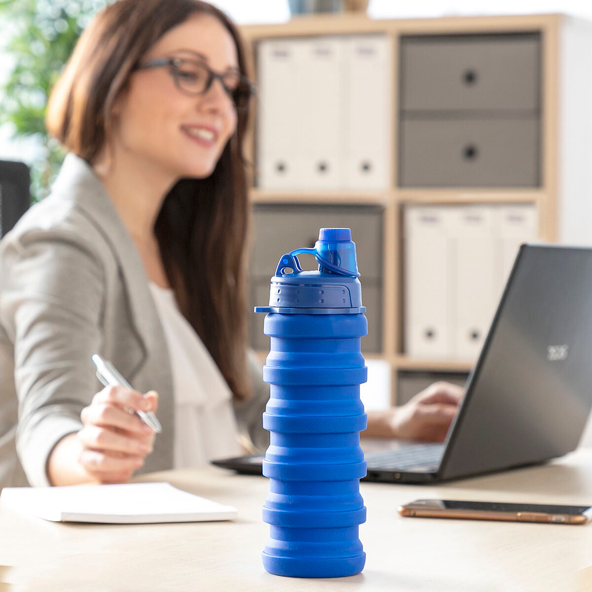 Einzelne blaue Bentle-Faltflasche auf einem Schreibtisch, Person und Laptop im Hintergrund